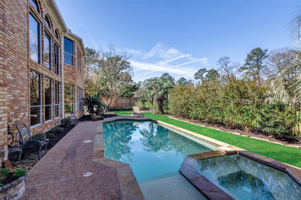 Spacious backyard with pool and spa had lush landscaping, bordered by a wooden fence on the sides and iron fence along the reserve in back. Beyond the fence, a serene view of tall trees and a clear blue sky creates a peaceful, private setting.