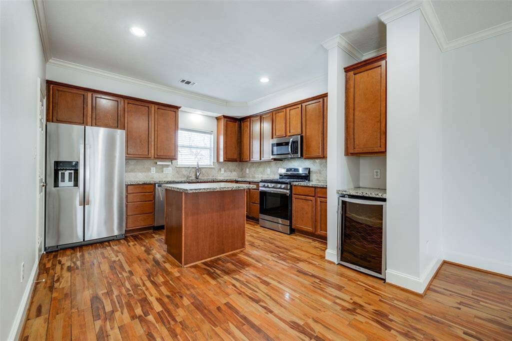 Kitchen has granite countertops, stone tile backsplash, plenty of cabinets space and center island with seating and storage. Dry bar with wine fridge and cabinet above to the right.