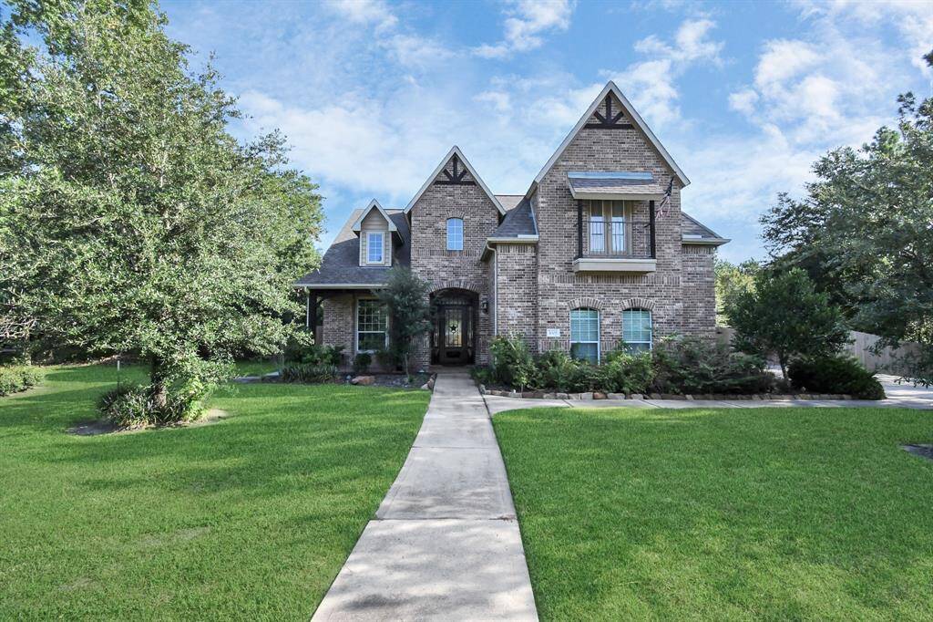 Charming two-story brick home with a well-manicured lawn and mature trees, featuring a welcoming walkway and an elegant arched entrance.
