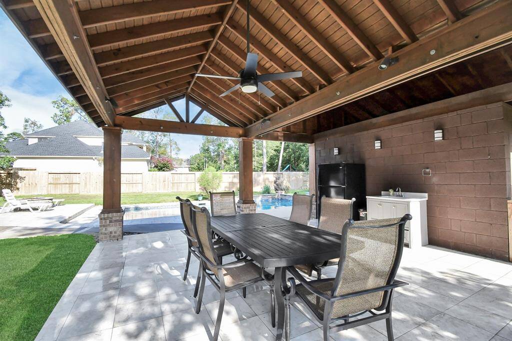 This is a spacious covered outdoor patio with a dining set overlooking a pool and private fenced yard, perfect for entertaining and al fresco dining.