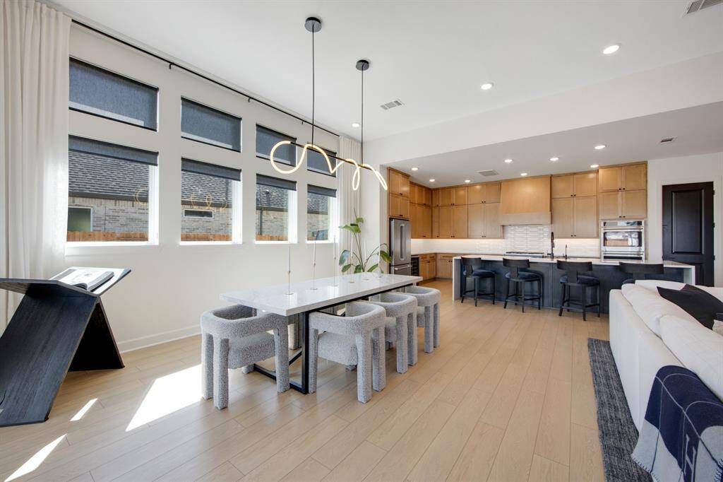The spacious dining area is illuminated by a stunning LED tube chandelier, creating a modern and vibrant atmosphere for meals and gatherings. Custom roller shades on the windows provide both privacy and light control, enhancing the room's comfort and style.