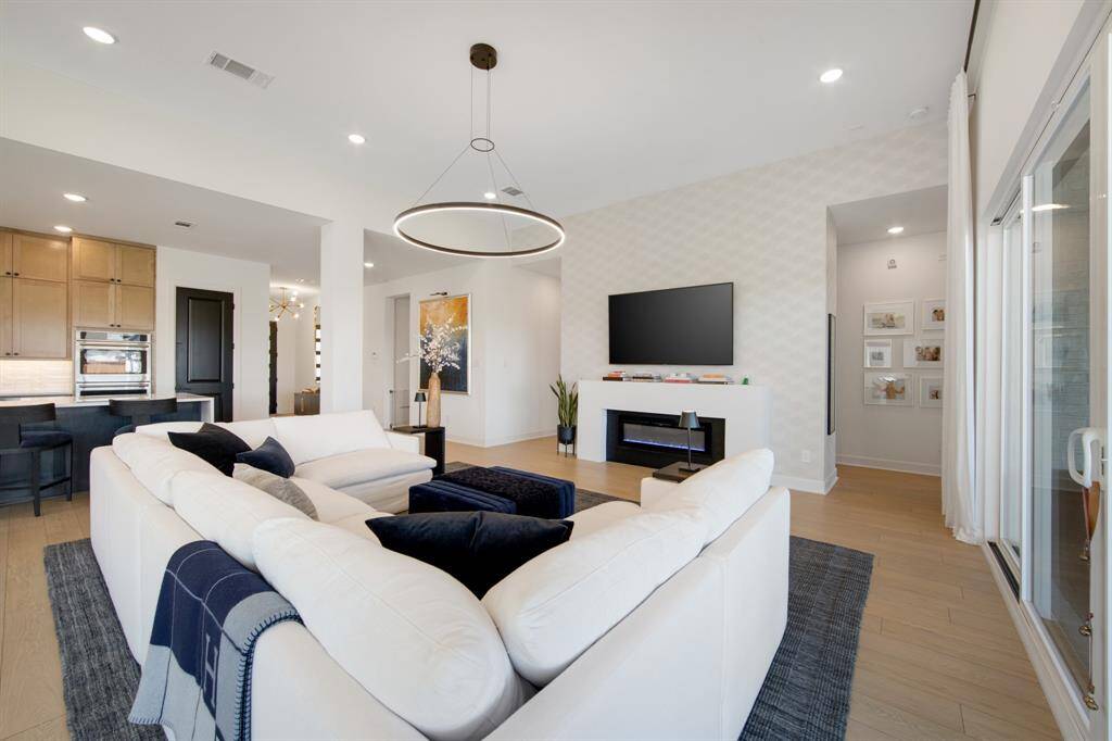The focal point of the living room is the custom contemporary fireplace, framed by luxurious Phillip Jeffries wallpaper that adds texture and elegance to the space. Above, a beautiful LED chandelier provides a soft, ambient glow, further enhancing the room’s stylish, sophisticated atmosphere.
