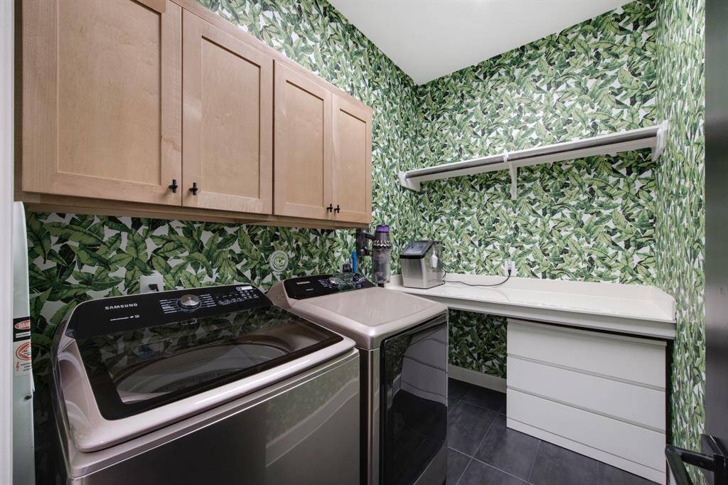 The laundry room is a stylish and efficient space, featuring built-in cabinets, a spacious counter, and a shelf for added storage and organization. The walls are adorned with Beverly Hills Hotel Palm wallpaper, adding a vibrant and sophisticated touch to the room.