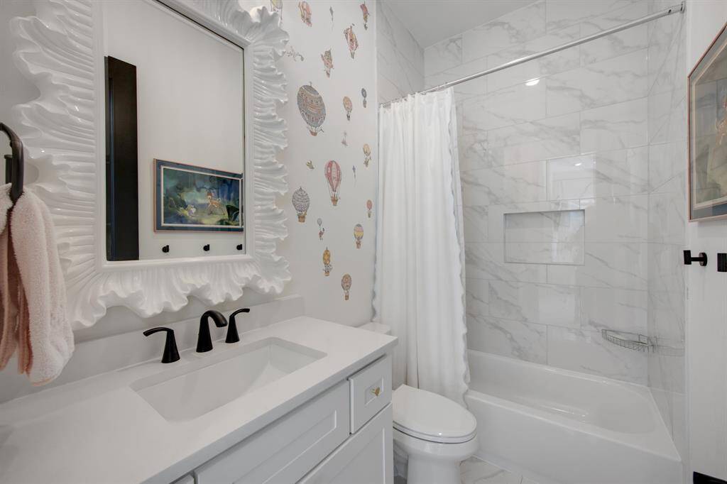 The secondary bathroom features a tub/shower combo, complemented by a framed mirror and upgraded fixtures, with a beautiful wallpaper accent on one wall that adds a touch of elegance and charm.