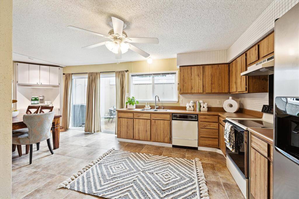 This is a well-lit kitchen with tile flooring, wood cabinetry, and a double sink. It features ample storage and modern appliances, with sliding doors leading to an outdoor space.