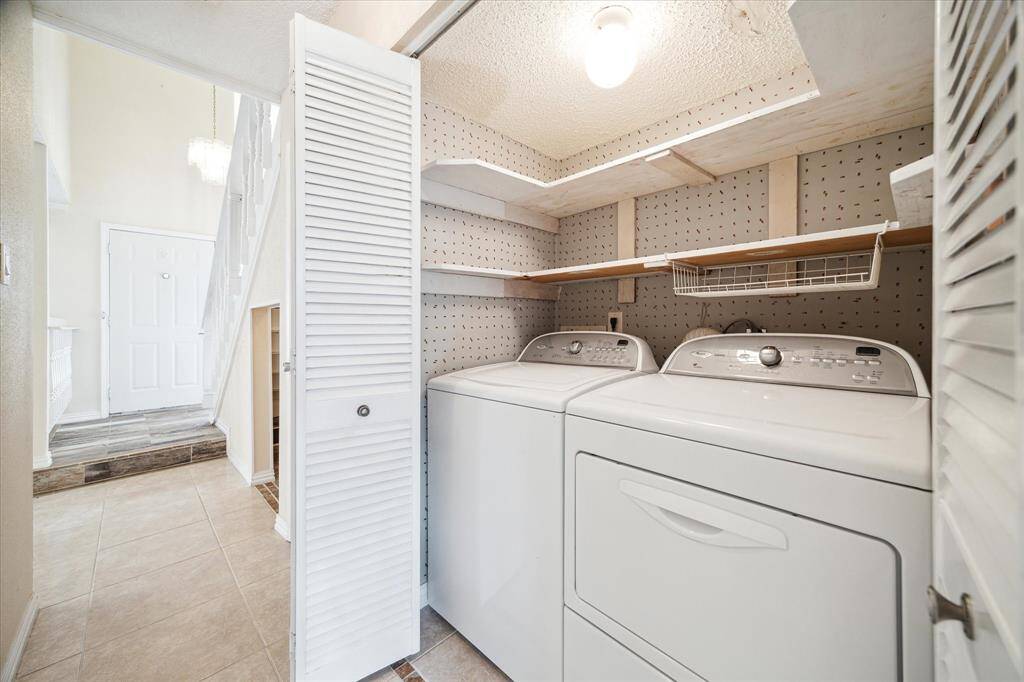 This laundry room features a washer and dryer, ample shelving for storage, and tiled flooring. It's conveniently located indoors on the first floor.