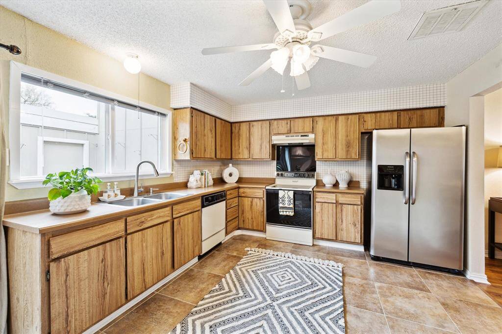 This is a bright kitchen with traditional wood cabinetry, tile flooring, a mix of vintage and modern stainless steel appliances, and a large window letting in natural light.