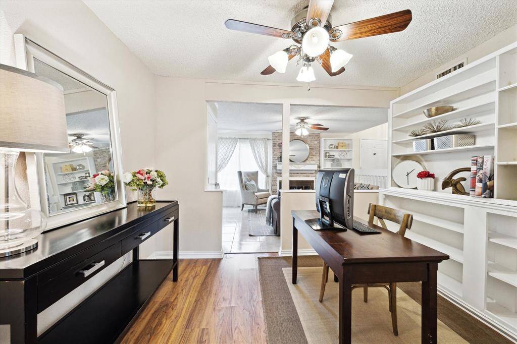 This is a well-lit, cozy living space currently used as a study featuring built-in white shelving for books or decor, and contrasting dark wood laminate flooring. This room could be a study, formal dining or additional living space.