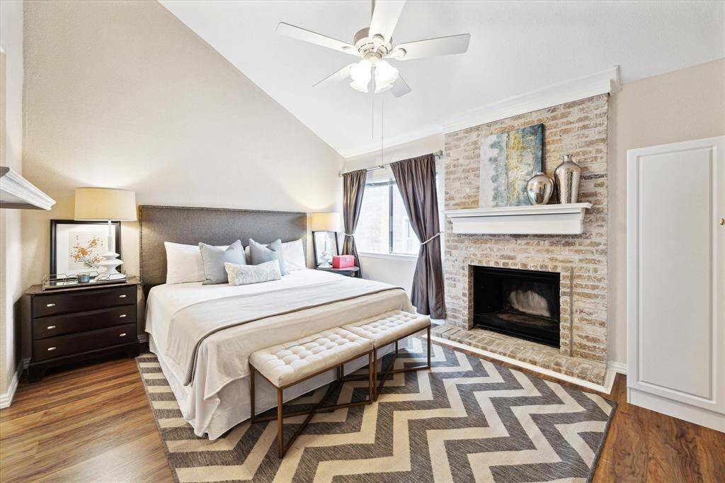 This is a bright, spacious 2nd floor primary bedroom featuring laminate wood flooring, a brick fireplace, large windows and high ceilings.