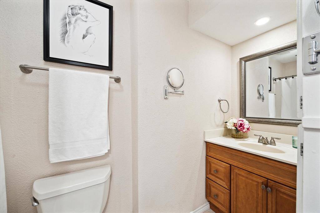 The primary bathroom features a wooden vanity with ample storage, topped with a white countertop and an undermount sink. Above the vanity is a framed mirror flanked by wall-mounted light fixture.