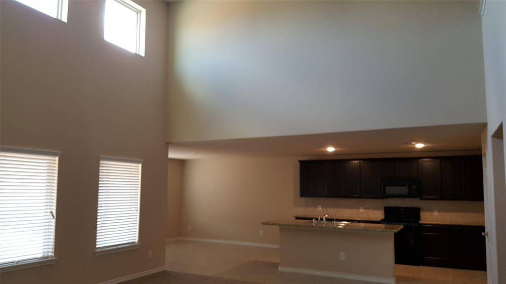 This photo showcases a spacious open-concept living area with high ceilings and abundant natural light from large windows. The kitchen features dark cabinetry and a countertop bar, offering a modern and inviting space. Perfect for entertaining and comfortable living.