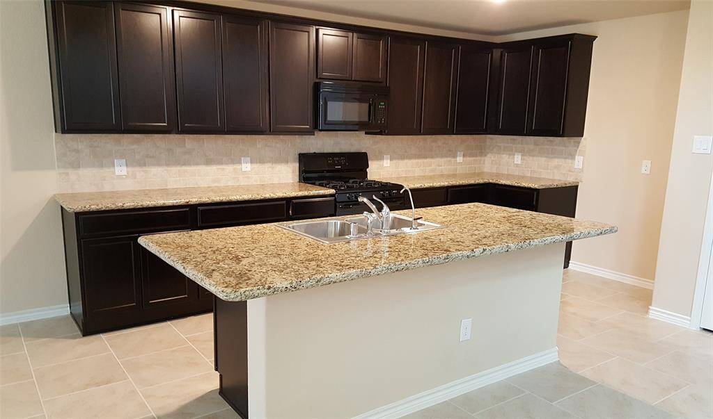 This kitchen features dark wood cabinets, granite countertops, a central island with a sink, and a modern appliance setup, offering a spacious and stylish cooking area.