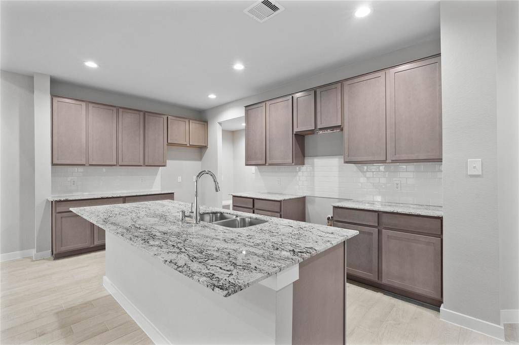 This kitchen is by far any chef’s dream! This spacious kitchen features high ceilings, stained wood cabinets, granite countertops, SS appliances, modern tile backsplash, recessed lighting, extended counter space, an island with double sink, and a walk-in pantry all overlooking your huge family room.