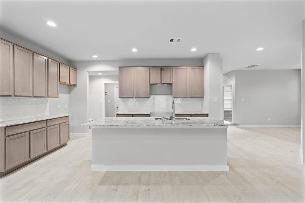 This kitchen is by far any chef’s dream! This spacious kitchen features high ceilings, stained wood cabinets, granite countertops, SS appliances, modern tile backsplash, recessed lighting, extended counter space, an island with double sink, and a walk-in pantry all overlooking your huge family room.