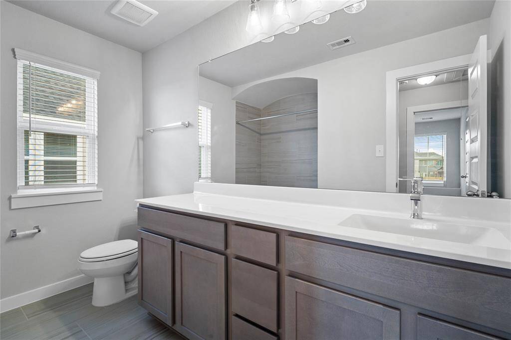 Secondary bathroom features light countertops and stained cabinets, custom paint, shower/tub combo with tile surround, large mirror, tile floors, sleek fixtures and modern finishes, plenty of space to accommodate any visiting family or guests.