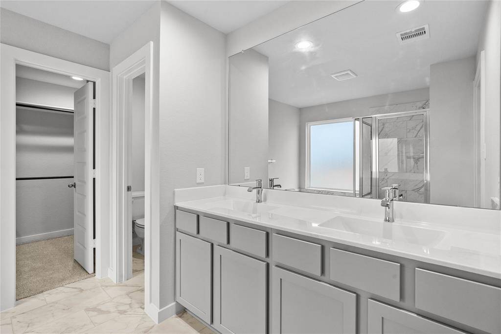 Wow! Look at this primary bathroom! Complete with stained cabinets and sleek light countertops with dual vanities, large modern tile flooring, walk in shower with tile surround, large soaking tub, and windows allowing in the natural light.