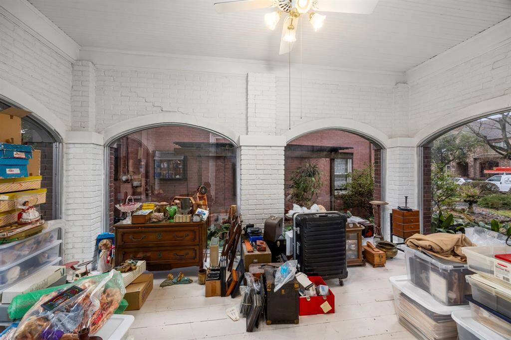 Sunroom with white brick walls and beautiful large arched windows, offering a bright and airy space. The room looks out onto the front yard with windows on all 3 sides.