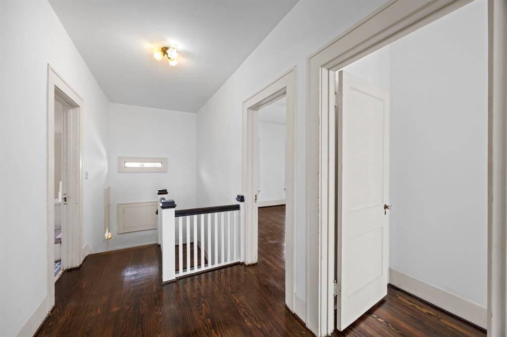 Well-lit hallway on the second floor with polished wood floors. It features several doorways leading to the different bedrooms.
