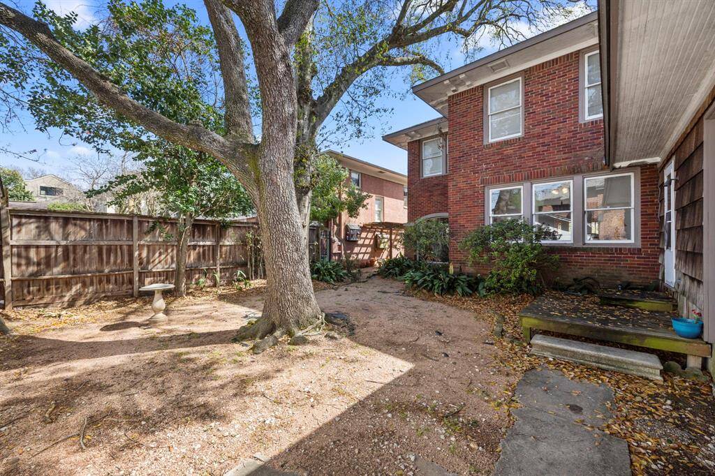 Charming backyard with a large tree providing shade, a wooden fence for privacy, and a brick exterior on the house. The space includes a small garden area with plants, making it ideal for outdoor relaxation.