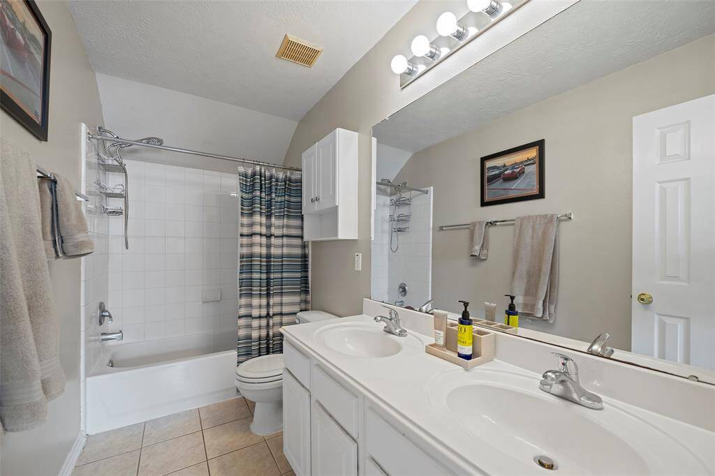 A large secondary that features a dual sink vanity with cabinets and drawers, and a shower/tub combination with tile surround!