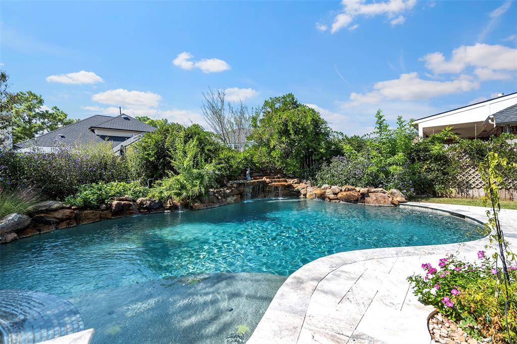 This pool features durable Pebble Sheen with LED lights and a relaxing waterfall surrounded by blooming foliage! The travertine decking and edging just compliments this pool so well!