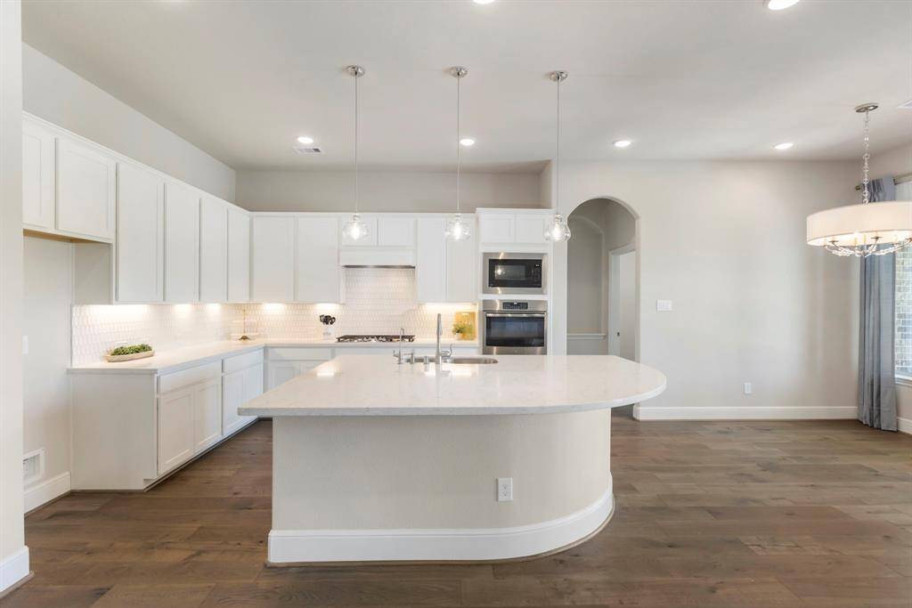 Check out all that storage! This stunning kitchen features a massive island with wraparound bar seating, elegant pendant lighting, quartz countertops, a designer backsplash, and undermount lighting!