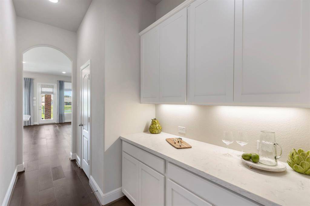 The butler’s pantry is perfectly positioned between the Formal Dining and Kitchen, featuring ample upper and lower storage, a quartz countertop, and undermount lighting.