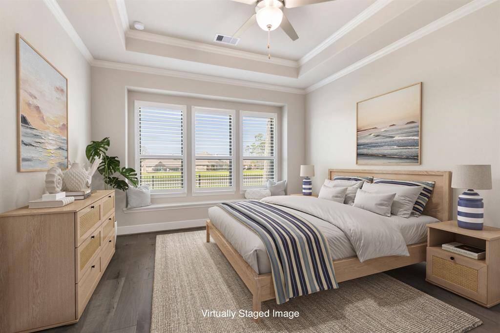 A truly relaxing retreat! The spacious Primary Bedroom features a wall of tall windows with stunning lake views, a charming window bench, plantation shutters, wood floors, and a tray ceiling with double crown molding. *Virtually Staged Image