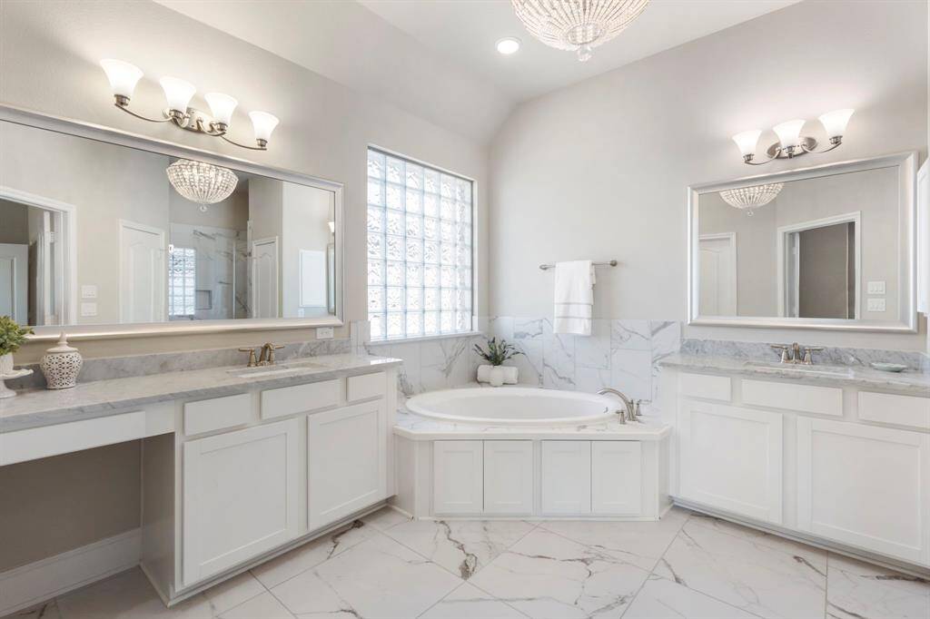 Upgraded features galore make this Primary Bath a spa-like experience! Stunning marble-like flooring, large soaker tub, with his/her vanities (one with seated area) double sinks, and crystal designer chandelier!
