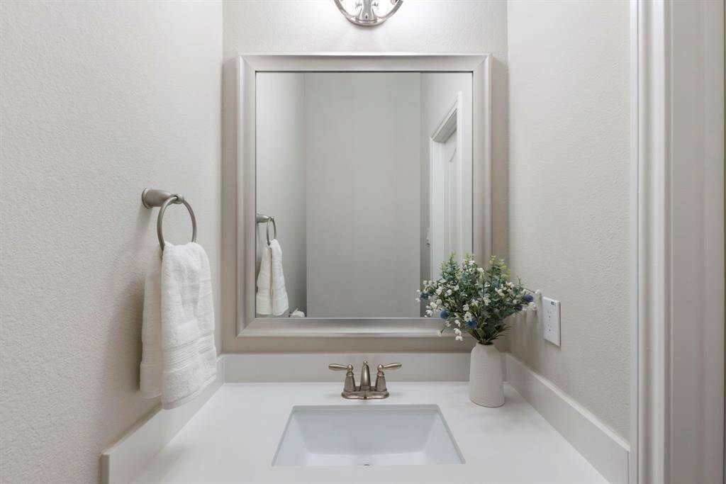 Powder bath, located off of foyer, features a quartz countertop and decorative mirror.