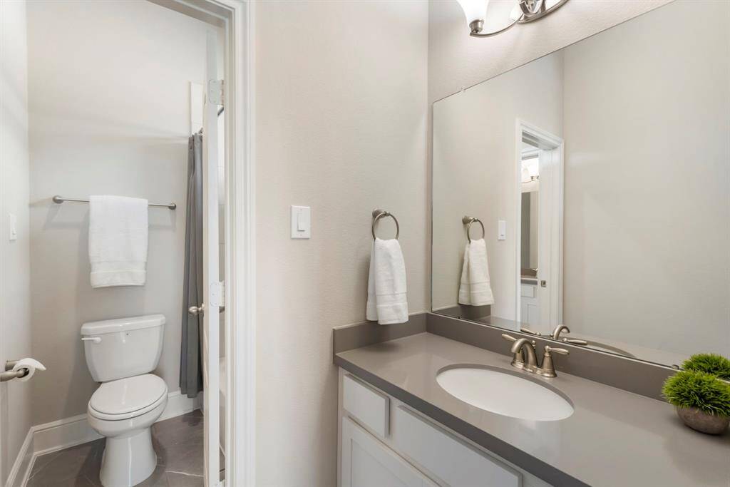 Beautifully appointed Jack-and-Jill bathroom with upgraded tile flooring and countertop with a shared private bath nestled between separate vanity areas.