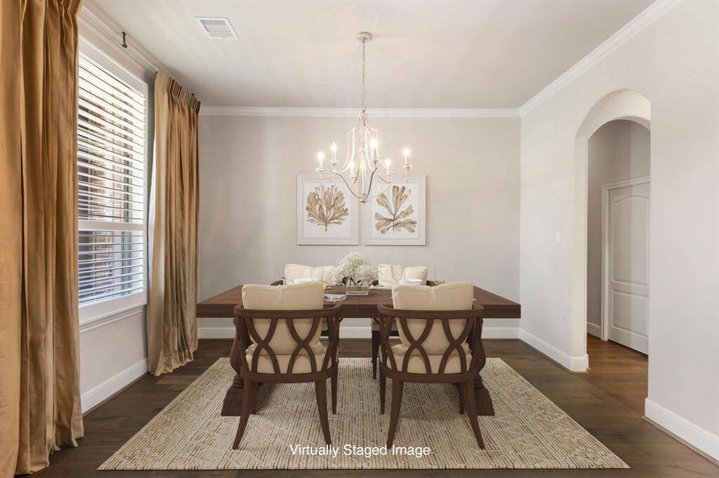 Elegant arched entry leads to the Formal Dining room, featuring wood flooring, a decorative chandelier, crown molding, and a convenient pass-through to the butler’s pantry. *Virtually Staged Image
