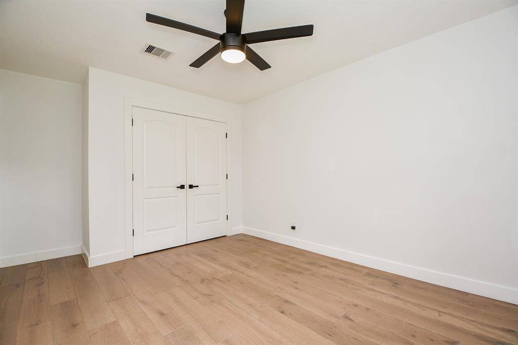 Spacious bedroom with elegant wood floors, ample natural light, and a sleek ceiling fan. Features a large closet with double doors for convenient storage.