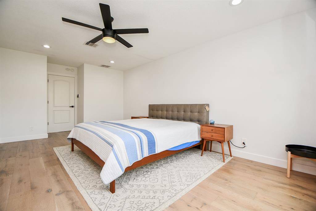 Spacious and bright primary bedroom featuring elegant hardwood floors, modern ceiling fan, and ample natural light for a serene retreat.