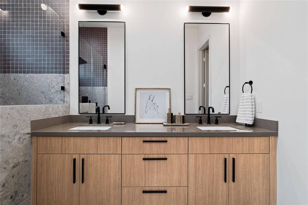 This primary bathroom showcases a seamless blend of modern design and functionality, featuring a spacious double vanity with sleek quartz countertops, custom wood cabinetry, and bold black hardware.