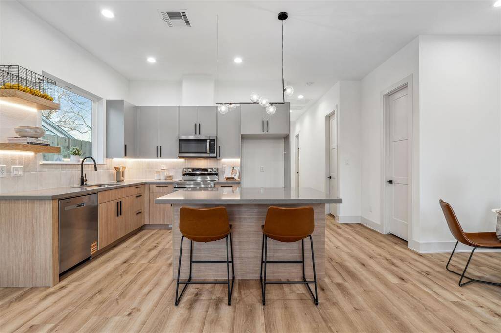 Stunning kitchen featuring sleek cabinetry, quartz countertops, and a spacious island with a gorgeous lighting feature. The open layout, warm flooring, and designer finishes make this the perfect space for entertaining.