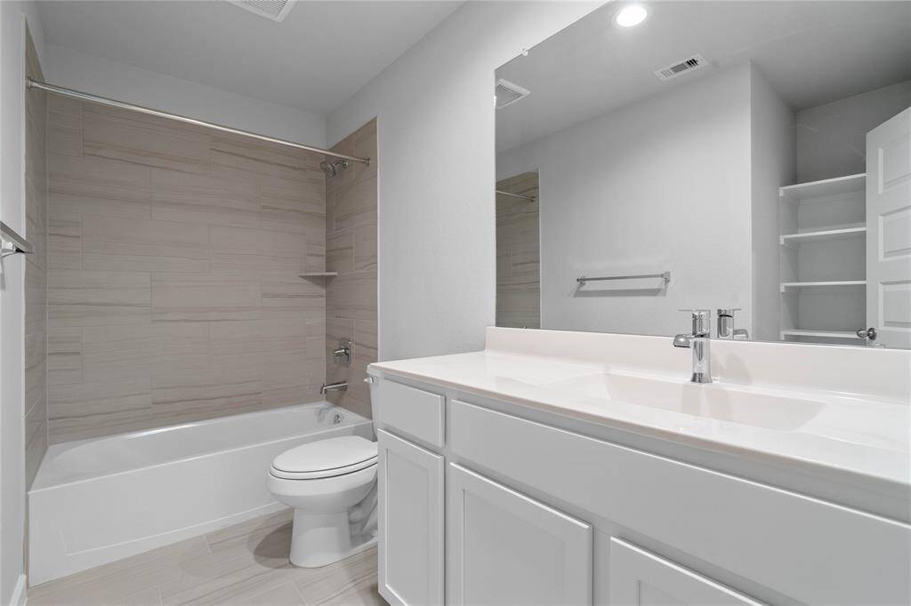 Secondary bath features tile flooring, bath/shower combo with tile surround, stained wood cabinets, beautiful light countertops, mirror, sleek fixtures and modern finishes!