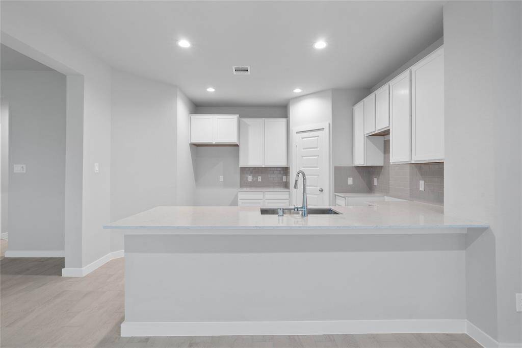 This stunning kitchen features stained cabinets, custom neutral paint, quartz countertops, modern backsplash, breakfast bar, recessed lighting, high ceilings, and walk in pantry!