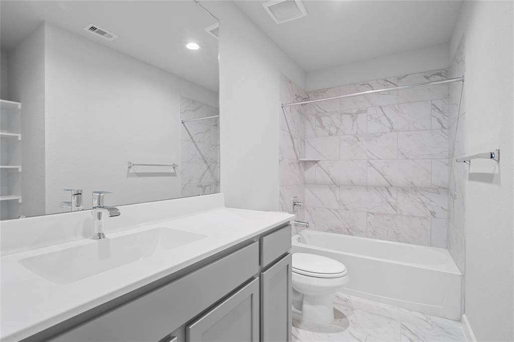 Secondary bath features tile flooring, bath/shower combo with tile surround, stained wood cabinets, beautiful light countertops, mirror, sleek fixtures and modern finishes!