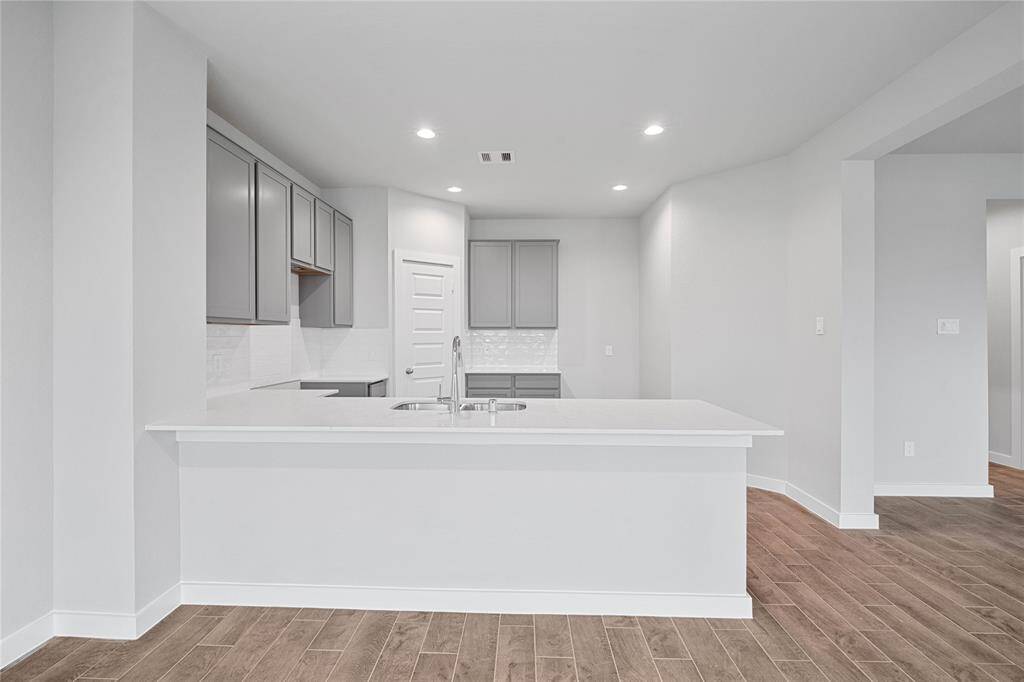 This stunning kitchen features stained cabinets, custom neutral paint, quartz countertops, modern backsplash, breakfast bar, recessed lighting, high ceilings, and walk in pantry!