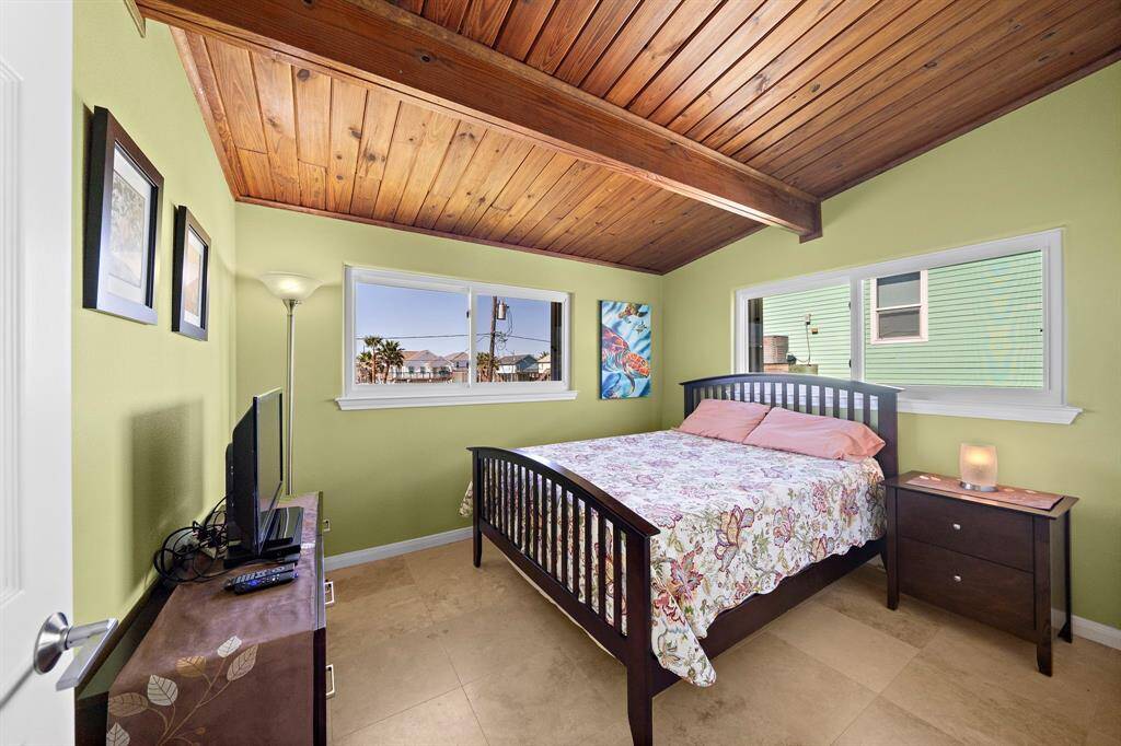 This charming bedroom features a warm wood-paneled ceiling, calming green walls, and natural light from multiple windows. The double-door closet offers convenient storage, while the simple design creates a restful space to unwind.