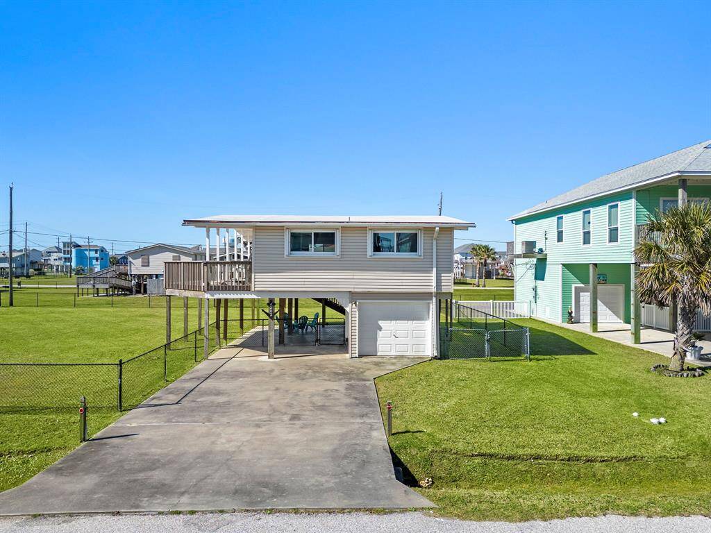 Front-facing view of the property featuring a long driveway, garage access, and fenced green space, all set on a quiet street.