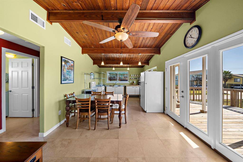 This open-concept layout features a light-filled living area with vaulted wood ceilings and tile floors, seamlessly flowing into the dining and kitchen space.