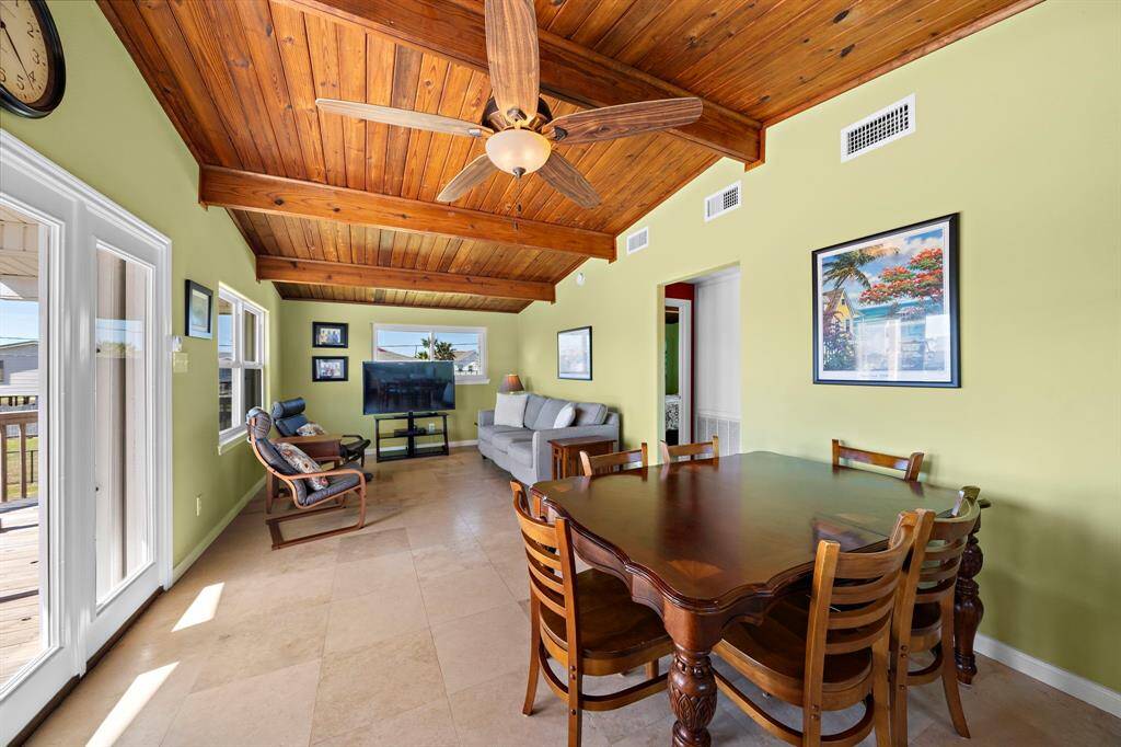 From the kitchen to the sofa, the open layout continues with warm-toned tile flooring and ceiling fans for coastal comfort. Natural wood beams and plenty of seating make this an inviting gathering spot.