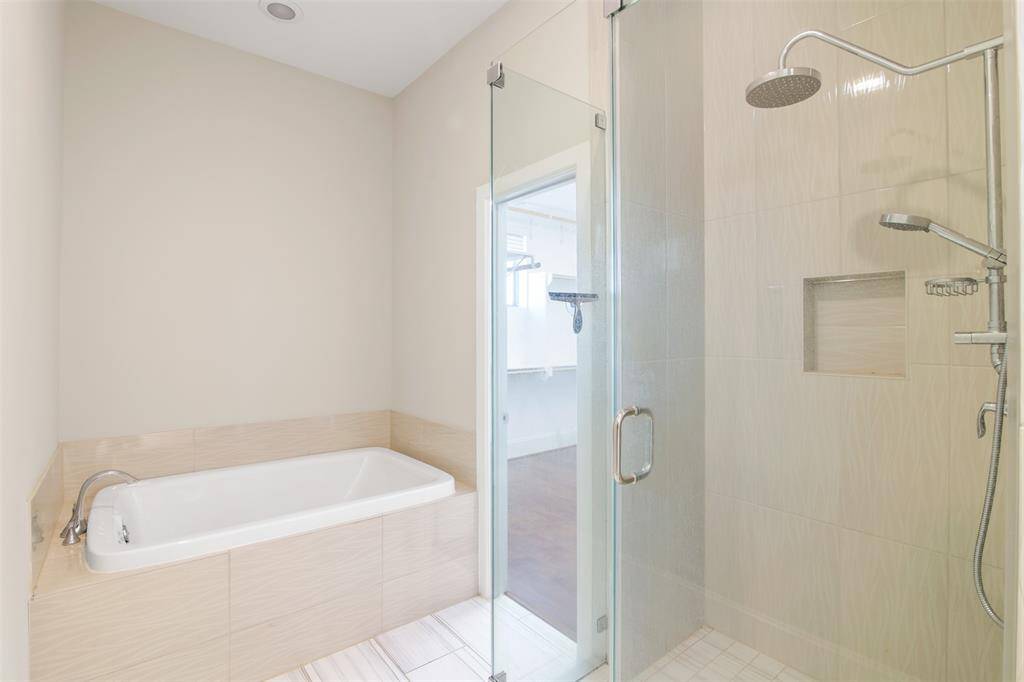 Frameless glass shower enclosure with tiled walls and double shower head shower, and a separate soaking tub.