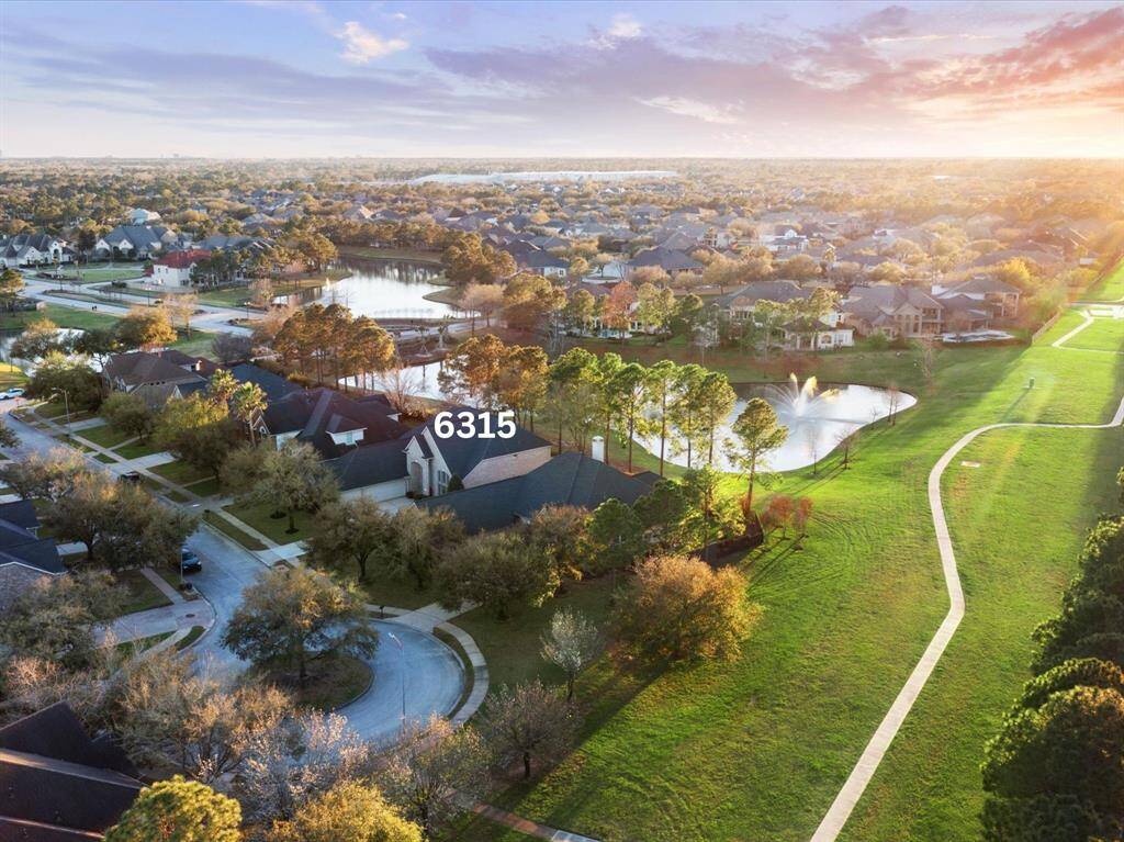 A stunning aerial view of 6315 Laguna Bay Ct showcases the home's prime lakefront cul-de-sac location. The walking path on the green space off the cul-de-sac leads to neighborhood amenities.
