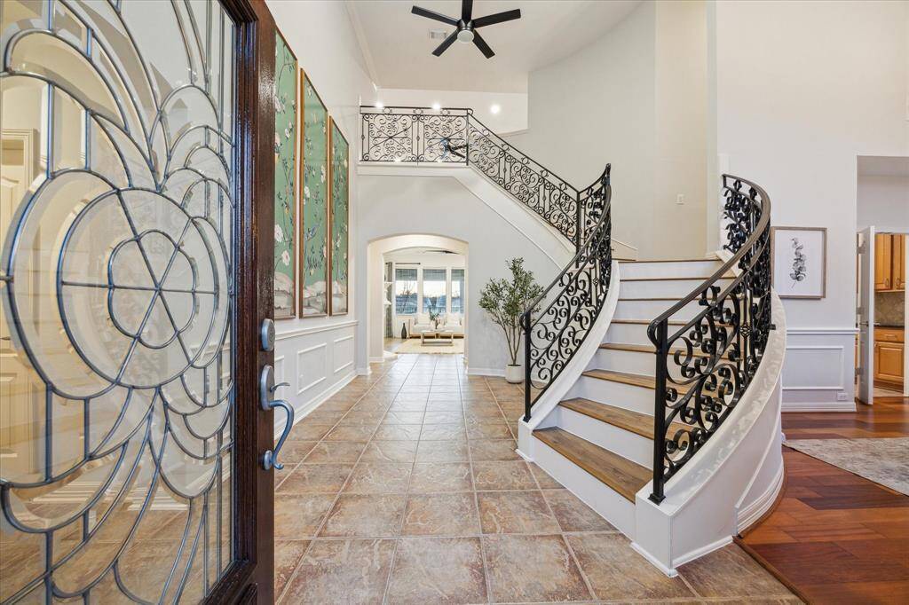 The elegant front door with glass insert opens to unveil a grand two-story foyer with a dramatic curved iron staircase.