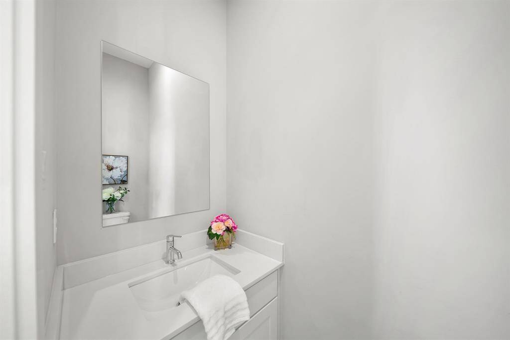 Tucked away on the second level of the home and convenient for guests is a half bath with a painted Shaker-style cabinet, quartz counter top with integrated back splash and under-mount sink, wall mounted mirror, recessed lighting & tile flooring.