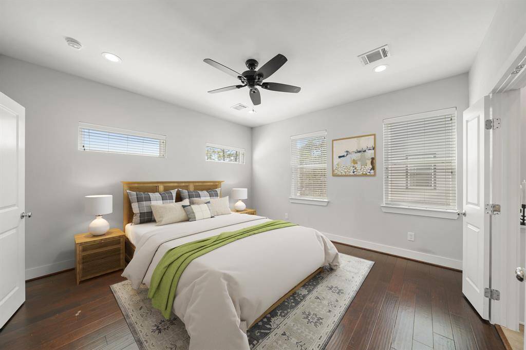 The owner's suite surrounded by windows with blinds has a high ceiling with recessed lights, ceiling fan with light fixture and beautiful hardwood floors. This photo has been virtually staged.