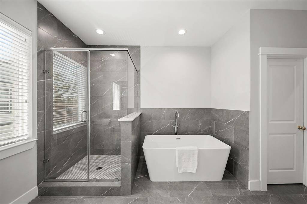 Relax and unwind in the free-standing soaking tub with floor mounted polished chrome plumbing fixtures surrounded by tiled accent walls and nearby floor-to-ceiling tile surrounded walk-in shower with frameless glass enclosure.